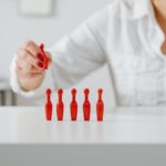 Close-up of a woman arranging red miniature bowling pins on a white tabletop indoors.