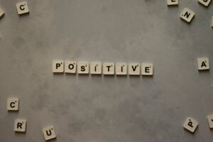 Scrabble tiles arranged to spell 'positive' on a gray textured surface, conveying optimism.