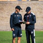 Two soccer coaches reviewing strategies on the field during the day.