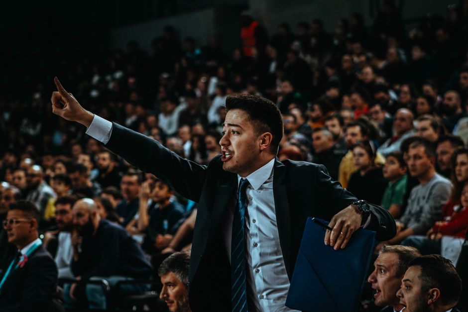Motivated coach directing during a tense basketball game in a crowded arena.