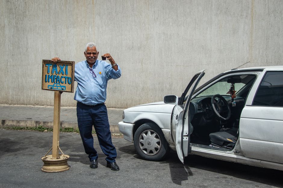 Senior man standing beside his taxi with an open door on a city street.